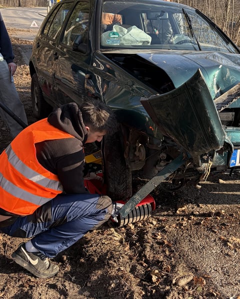 Emergency responder in orange vest examining severely damaged black car after accident