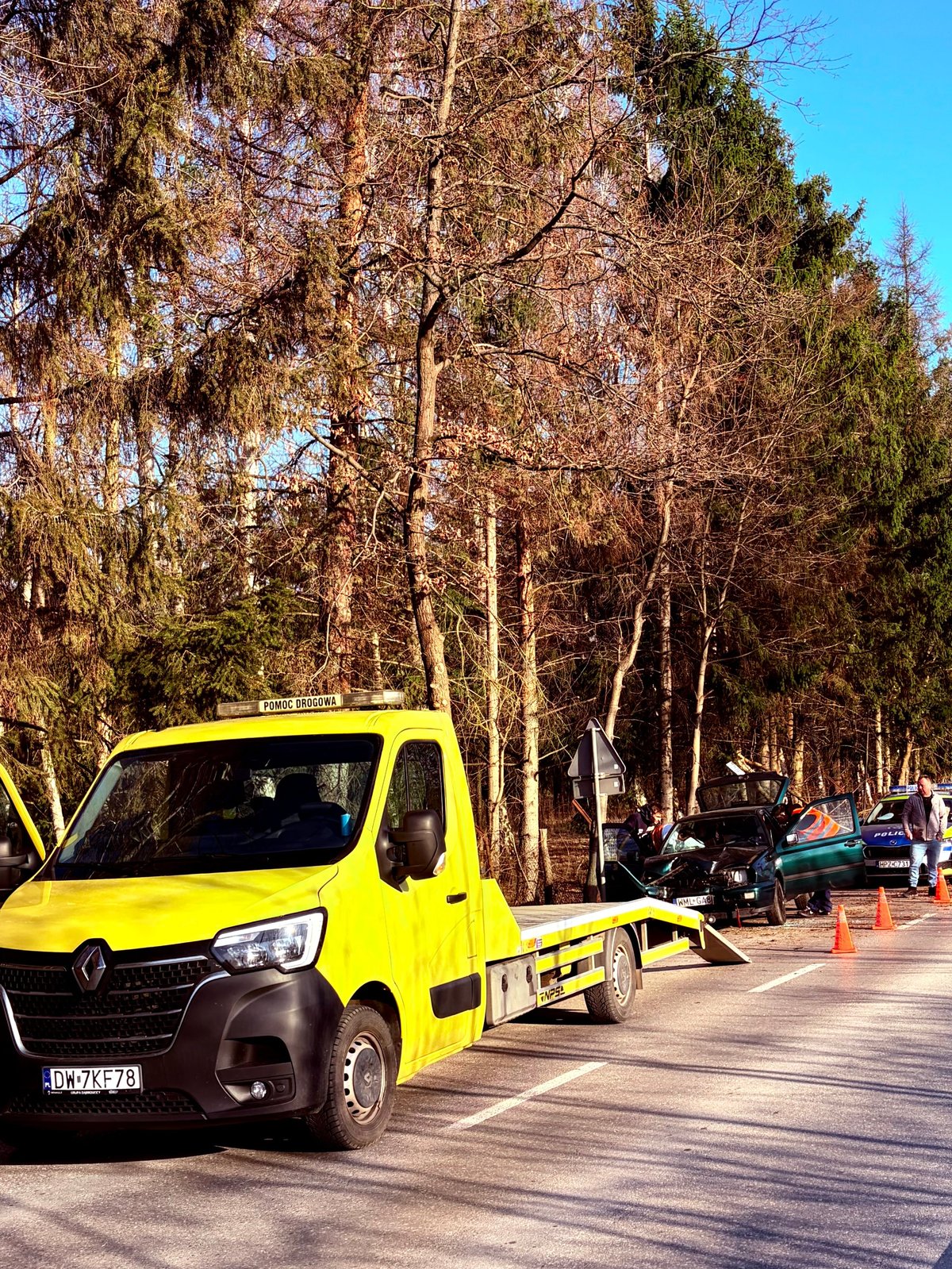 Yellow Renault tow truck parked on a street lined with bare birch trees and autumn foliage in background